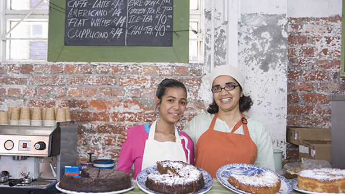 Portrait of happy mother and daughter in aprons standing at cake shop counter