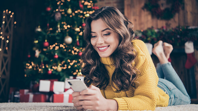 Young woman in front of Christmas tree shopping on her cell phone